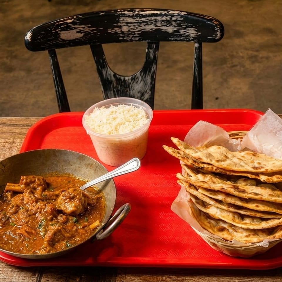 A red tray with a bowl of curry, a container of rice, and a basket of naan bread.