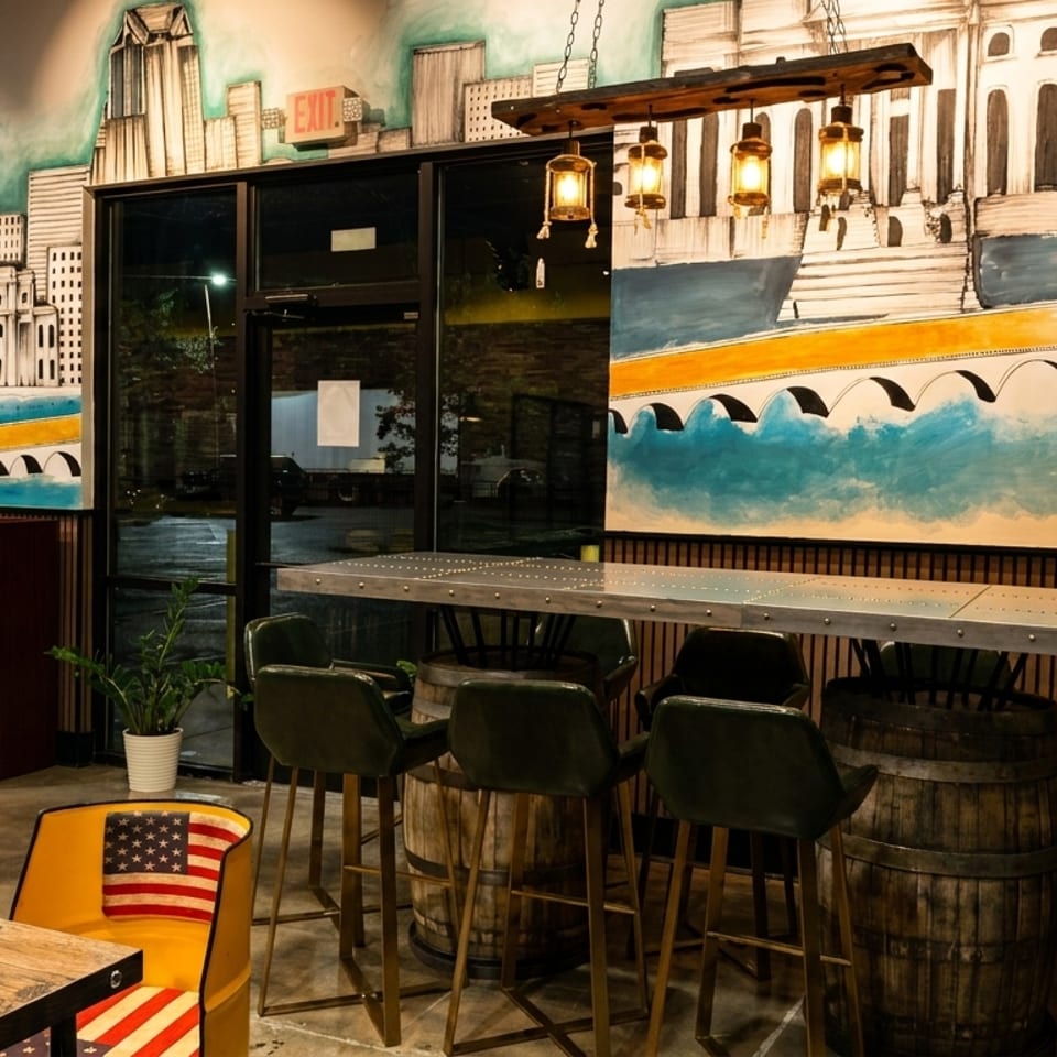 Restaurant interior with a large mural of a city skyline, bar seating, and dining tables.