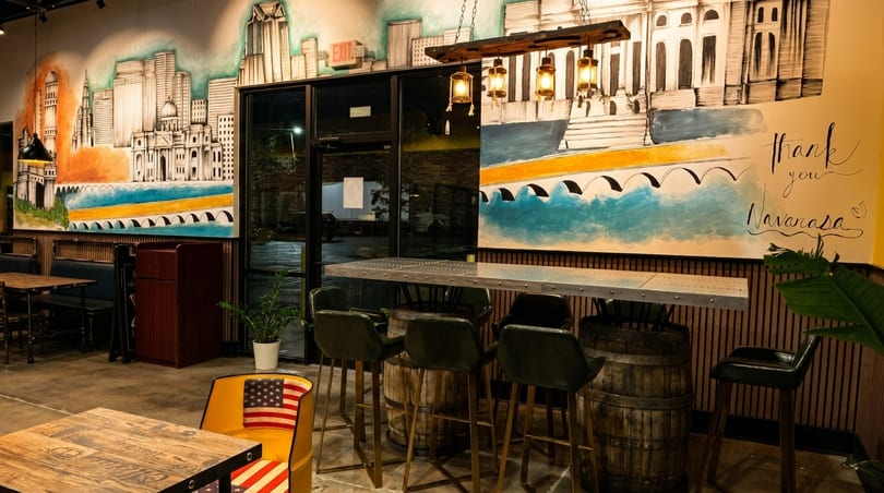 Restaurant interior with a large mural of a city skyline, bar seating, and dining tables.