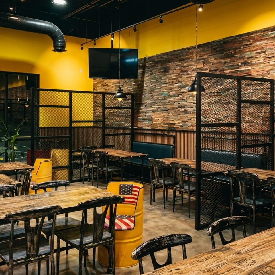 Restaurant interior with yellow walls, wooden tables, metal chairs, and booth seating against a brick wall.